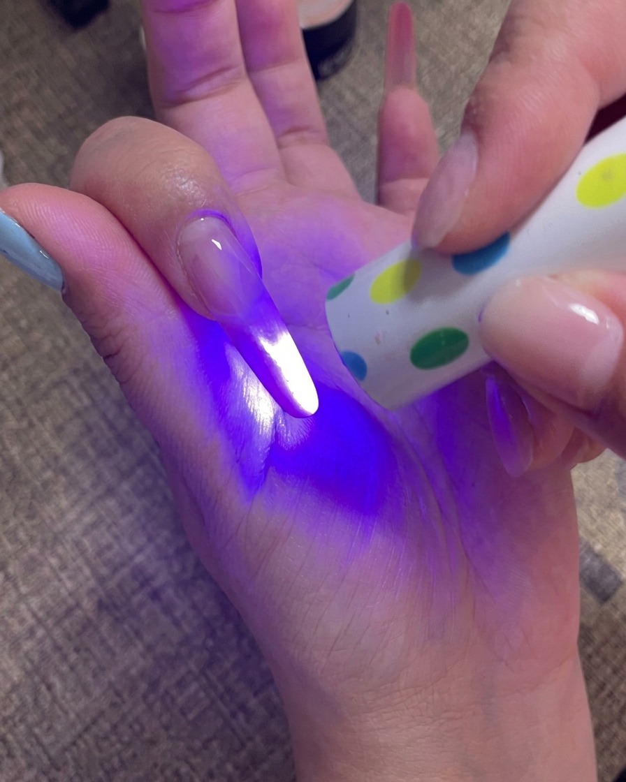 Una mano sosteniendo una lámpara UV portátil directamente sobre las uñas para curar la capa final de gel.