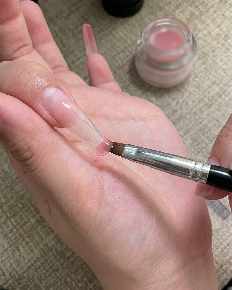 Un pincel de nail art aplicando y difuminando gel en la punta de la uña.