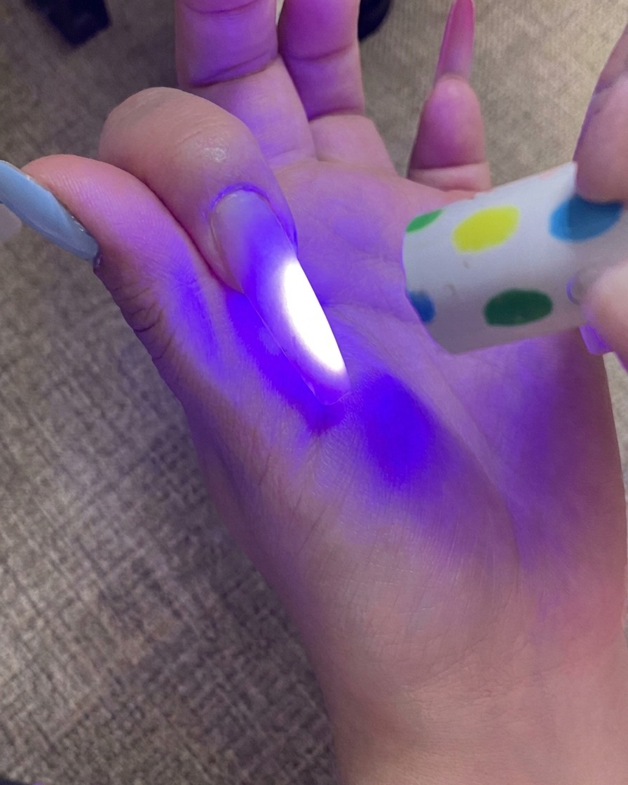 Una mano curando la uña con punta ombré bajo una lámpara UV, con la luz iluminando la uña.