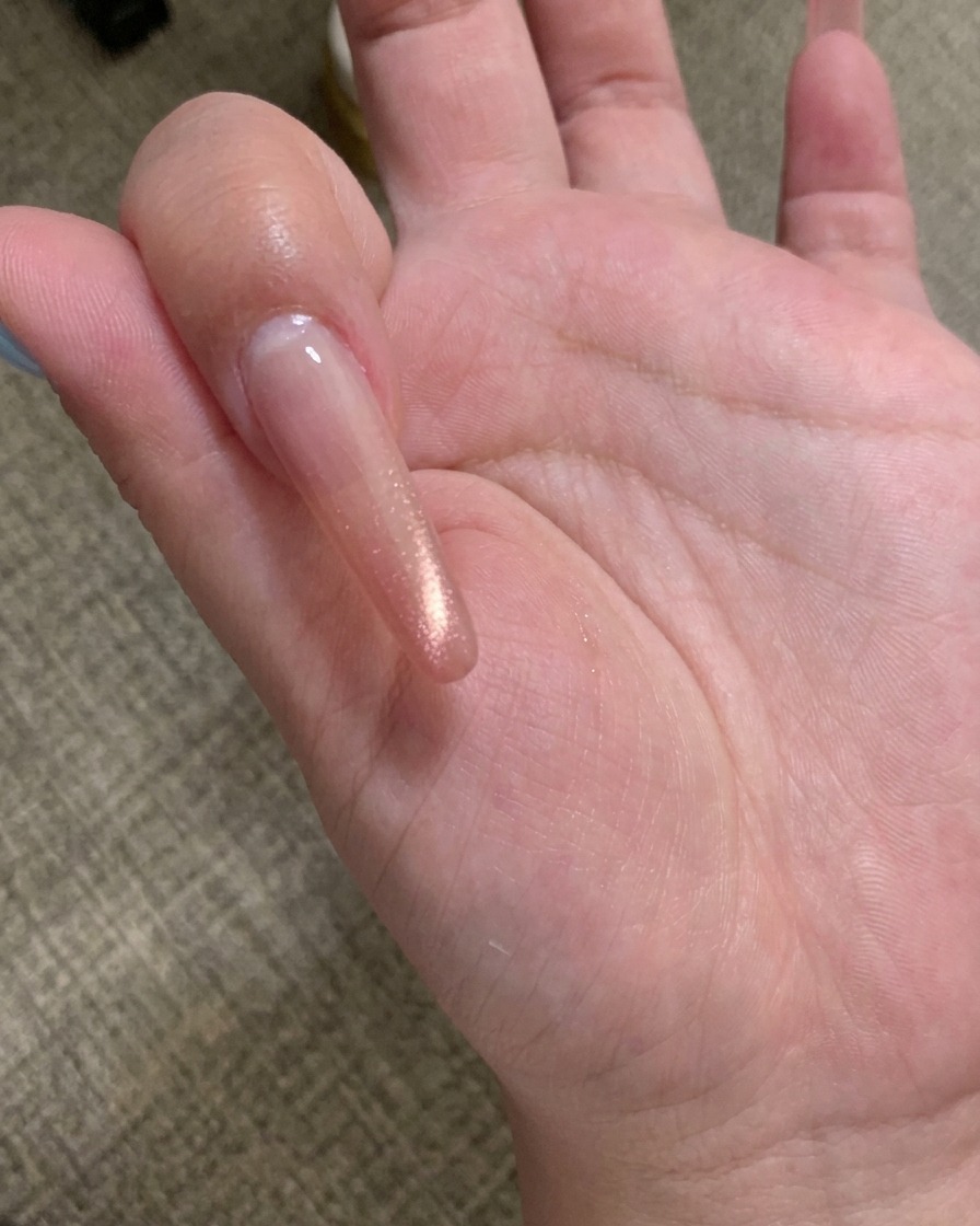 Primer plano de una herramienta magnética sostenida sobre una uña cubierta con gel ojo de gato color champán, mostrando las partículas agrupándose en una línea.