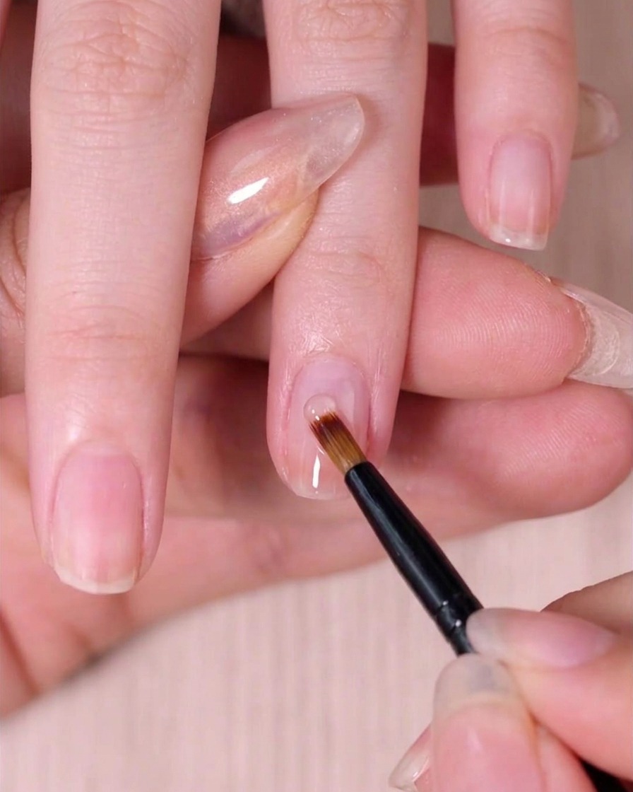 Un pincel especial para uñas difuminando ligeramente el esmalte rosa húmedo hacia abajo para crear un efecto ombré.