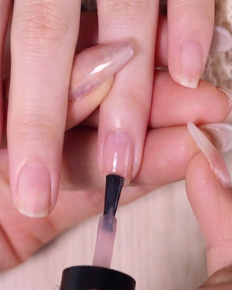 Un pincel aplicando una segunda capa de esmalte rosa nude en la mitad superior de la uña sobre una capa previamente difuminada.