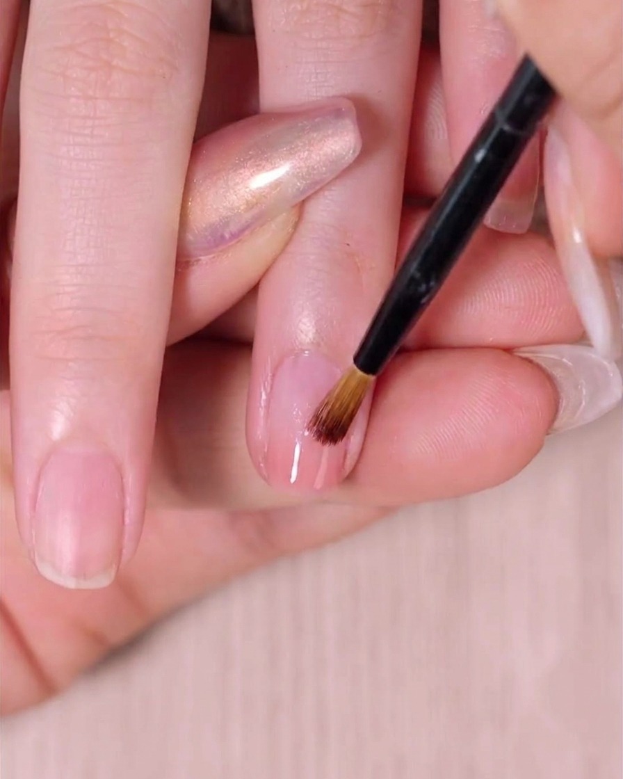 Un pincel para ombré barriendo suavemente la segunda capa de esmalte rosa para perfeccionar el degradado en la uña.