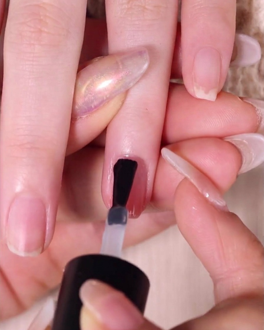 Un pincel aplicando una capa gruesa y brillante de esmalte final transparente sobre una uña ombré rosa terminada.