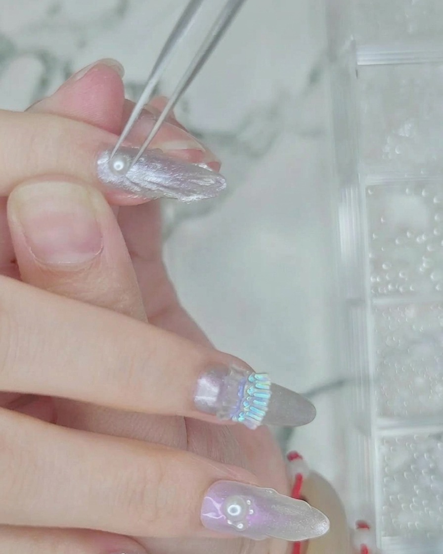 Unas pinzas colocando pequeñas perlas blancas sobre una línea de gel transparente húmedo en la uña.