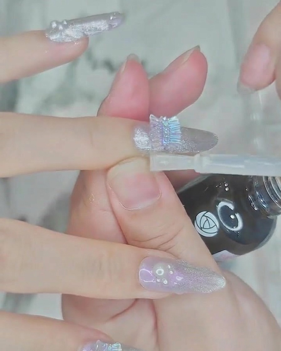 Un pincel aplicando una capa de top coat transparente y brillante sobre la uña y las decoraciones de perlas.