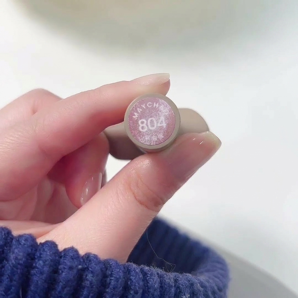 Primer plano de una mano sosteniendo el frasco de Meichao 804 Taozhi Yaoyao mientras se aplica el esmalte rosa nude brillante sobre una uña.