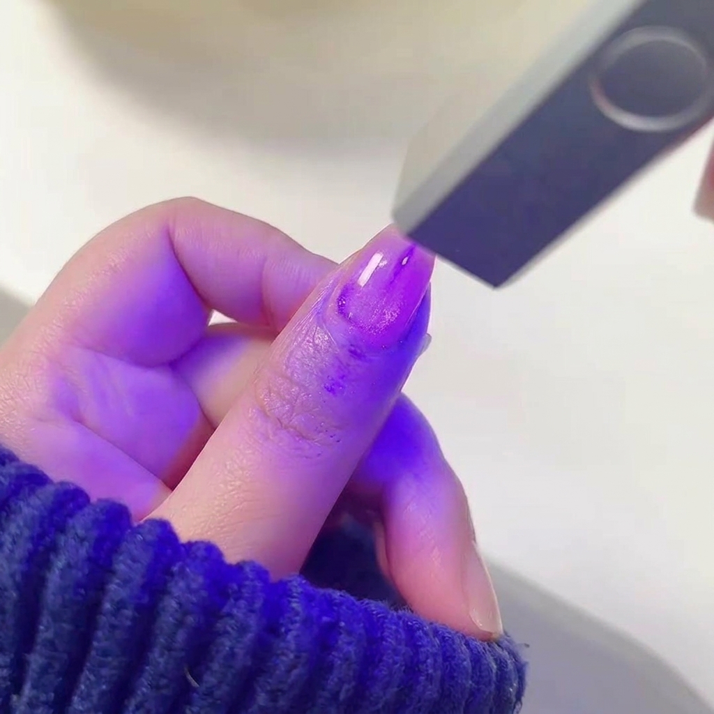 Un dedo con esmalte gel morado brillante húmedo posicionado dentro de una lámpara UV/LED para uñas.