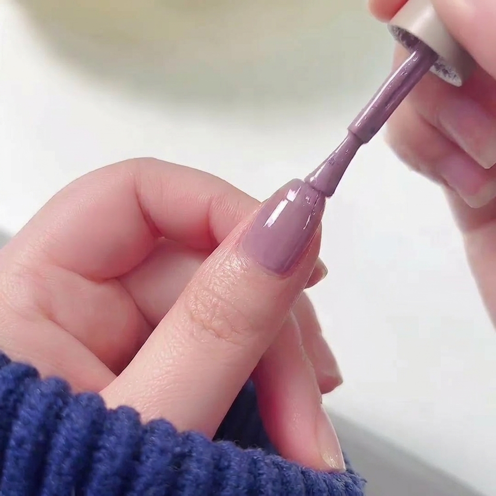 Un pincel de esmalte aplicando gel morado en la mitad superior de una uña sobre una base rosa.