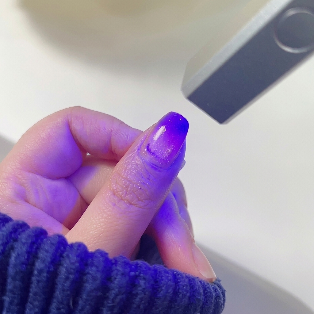 Una uña con un degradado de rosa y morado difuminado curándose bajo la luz morada de una mini lámpara LED.