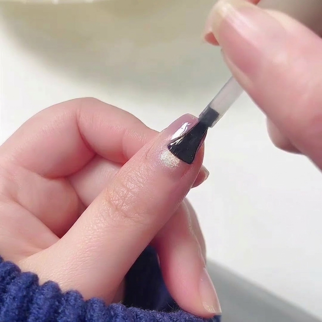 Un pincel aplicando un top coat transparente de alto brillo sobre la superficie de una uña con el diseño degradado.
