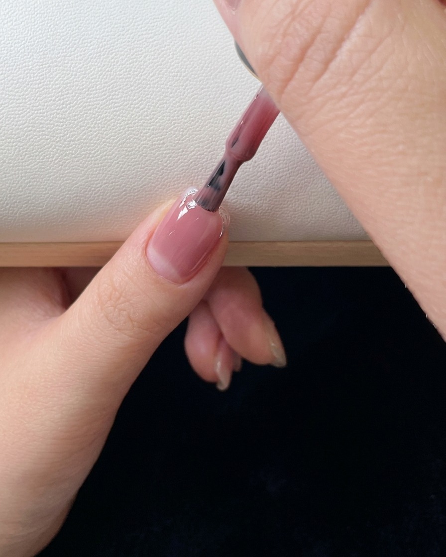 Primer plano de un pincel aplicando una segunda capa de gel rosa y difuminando el color por la uña.