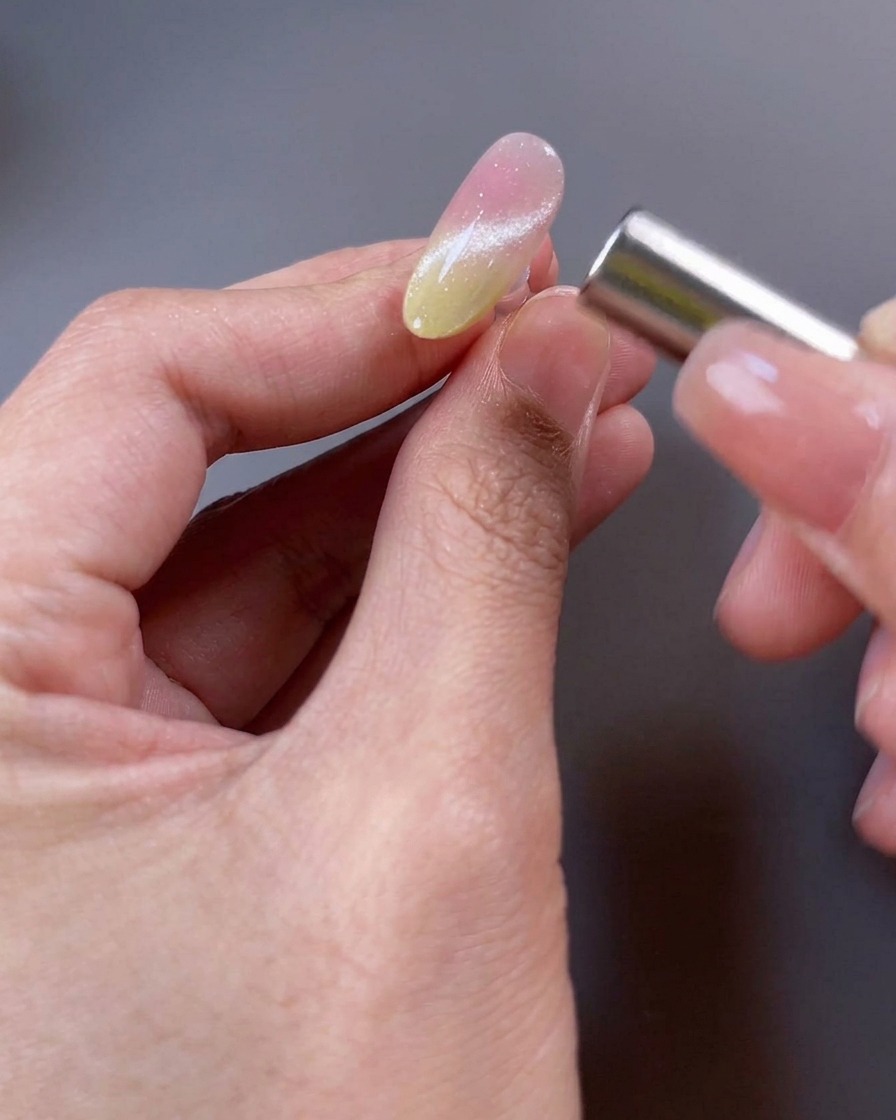 Primer plano de una uña con esmalte magnético y un imán cerca de la superficie manipulando las partículas para formar un haz de luz amplio.