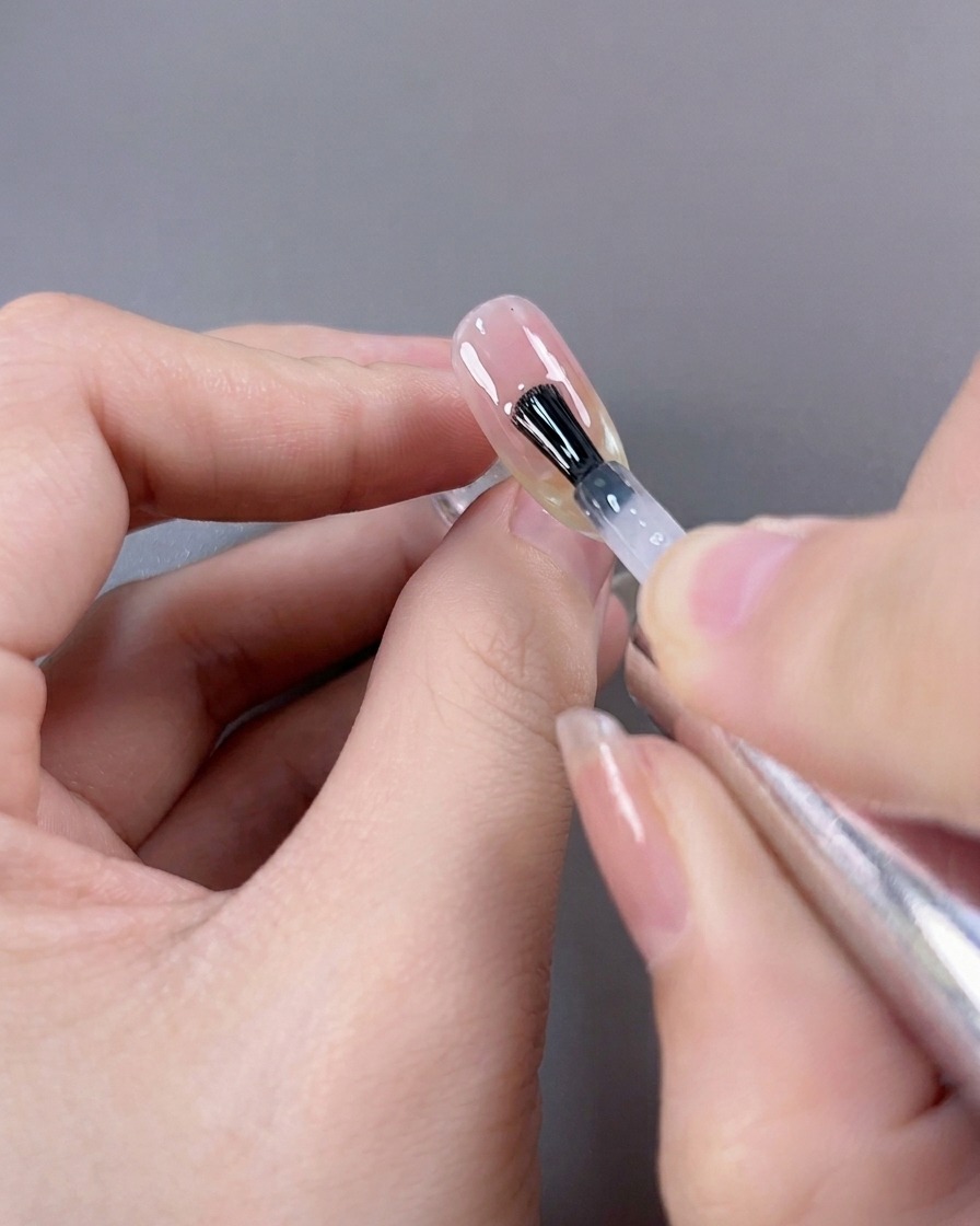 Un pincel aplicando una capa final de top coat de alto brillo sobre una manicura francesa de ojo de gato terminada.