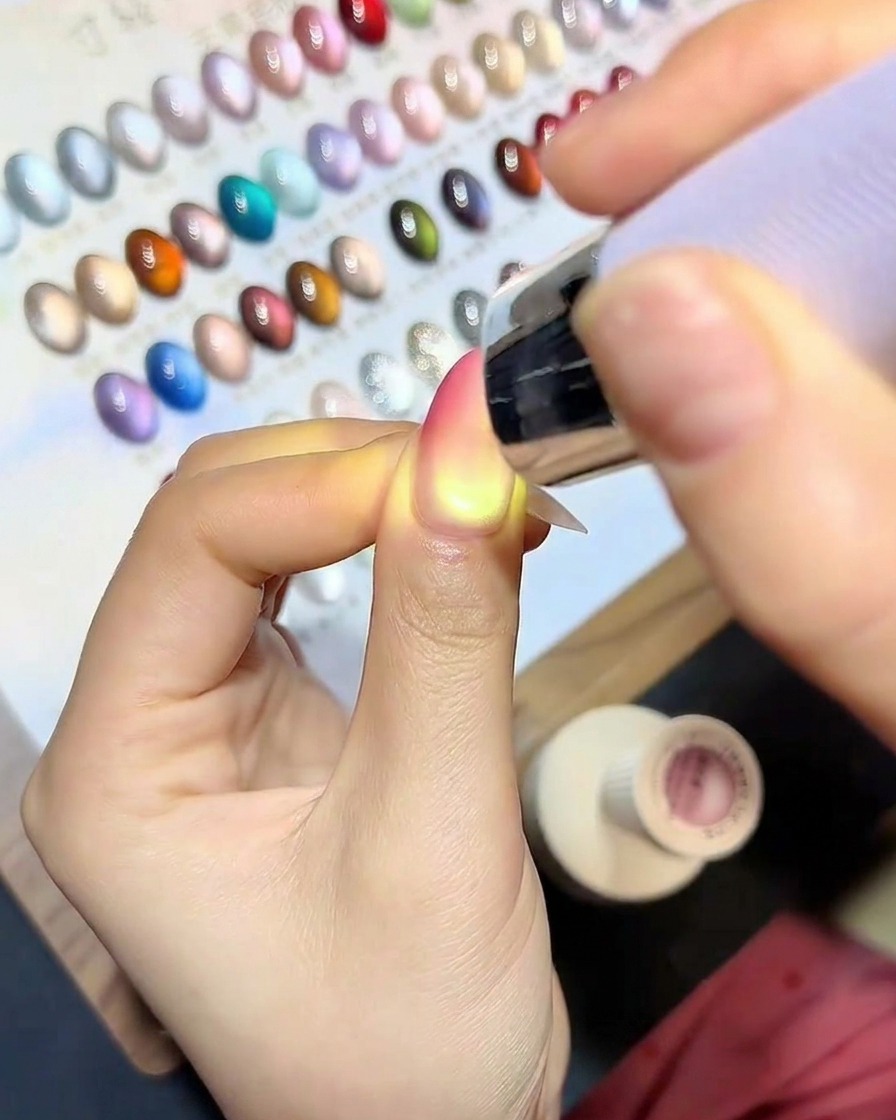 Un pincel aplicando un top coat transparente y brillante sobre la uña terminada con degradado y ojo de gato.