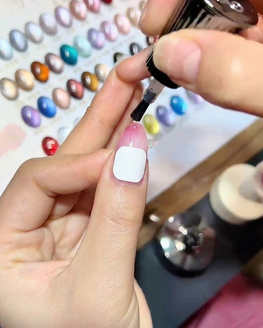 Vista de cerca de una mano con el top coat recién aplicado descansando dentro de una lámpara de uñas UV profesional, con luz azul iluminando las uñas.