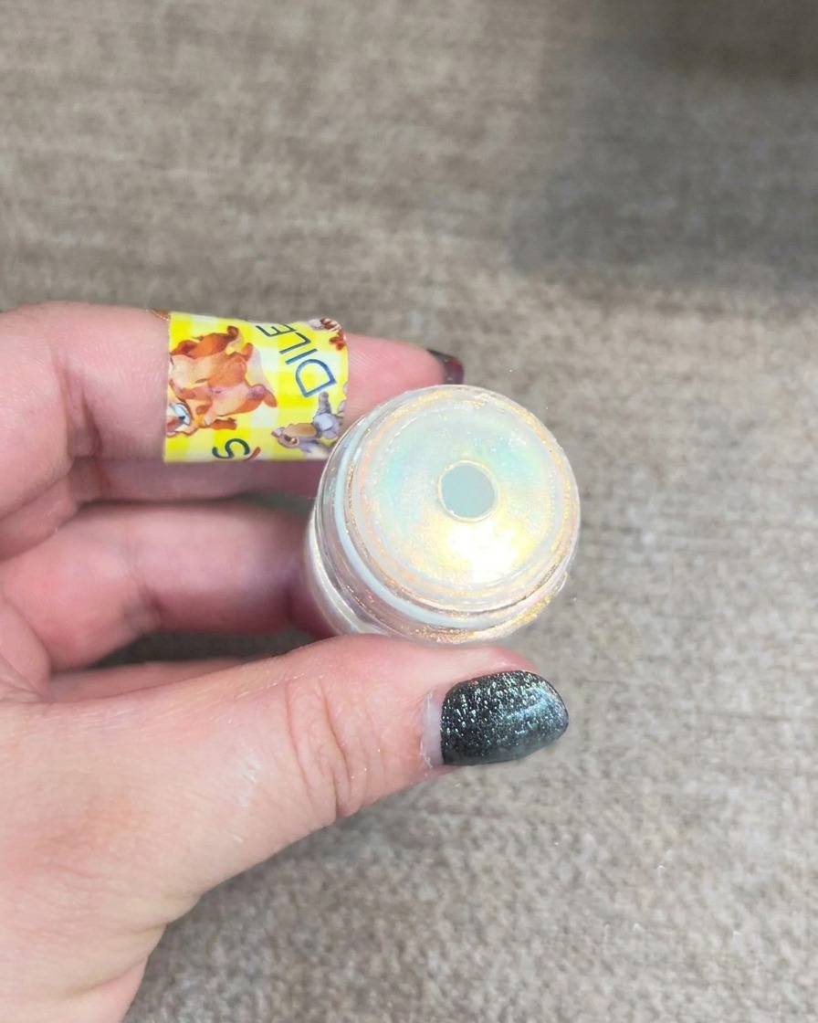 Un pequeño frasco de polvo aurora para uñas mostrando destellos amarillos y azules multidimensionales.