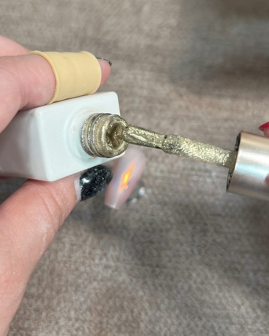 Pincel de uñas aplicando pequeños puntos de gel ojo de gato dorado brillante sobre una uña parcialmente decorada.