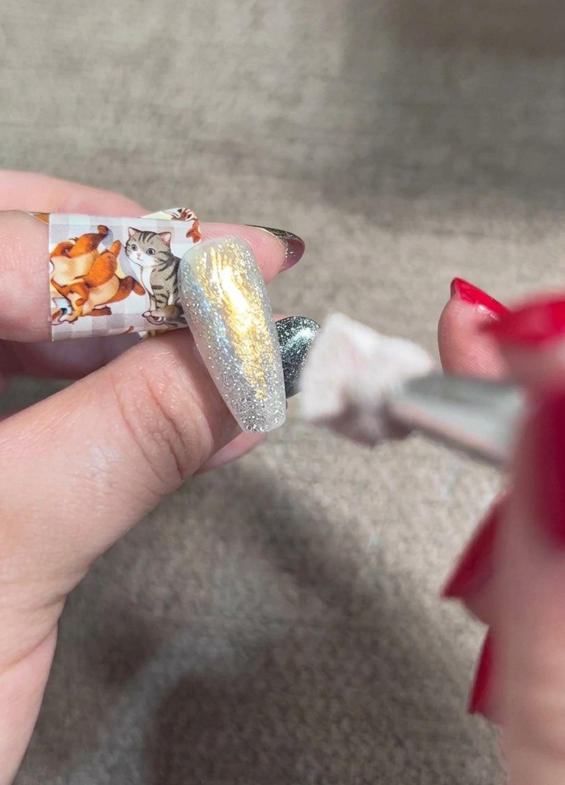 Un pincel de difuminado aplicando gel naranja blush sobre una uña brillante y multicolor para crear un degradado suave.