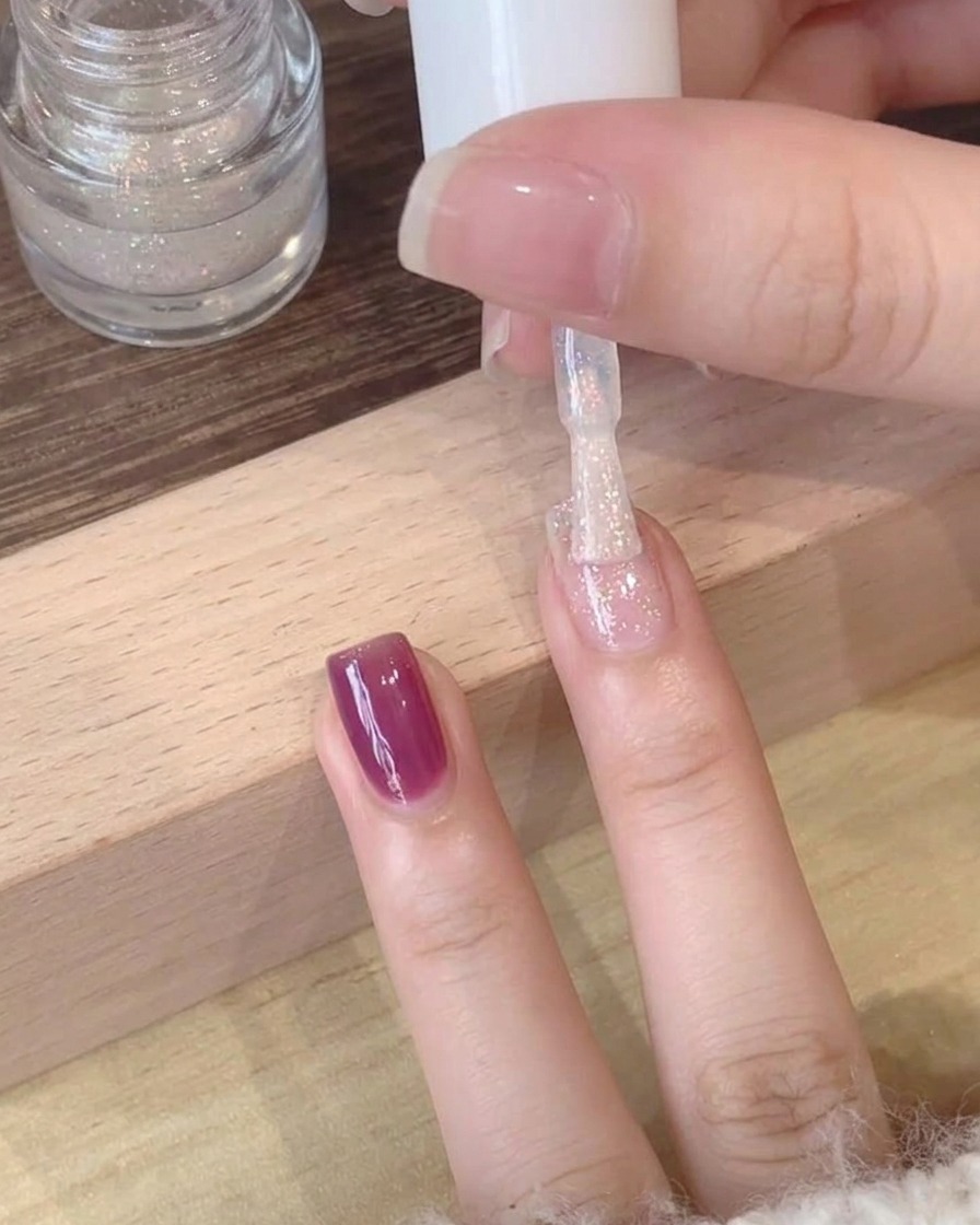 Vista en primer plano de un esmalte superior brillante y polarizado siendo aplicado sobre una base de gel púrpura profundo.