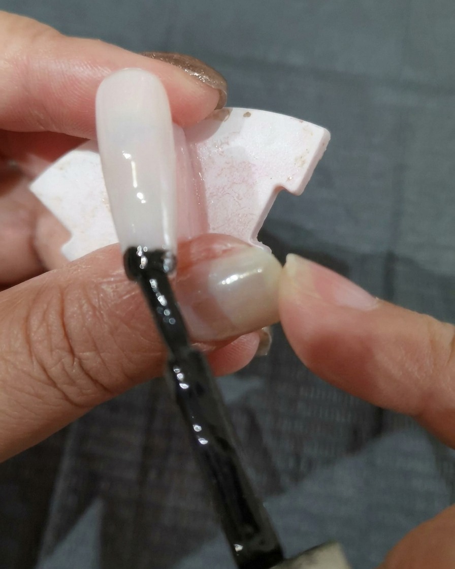 Pincel aplicando una capa de esmalte de gel negro sobre una uña.