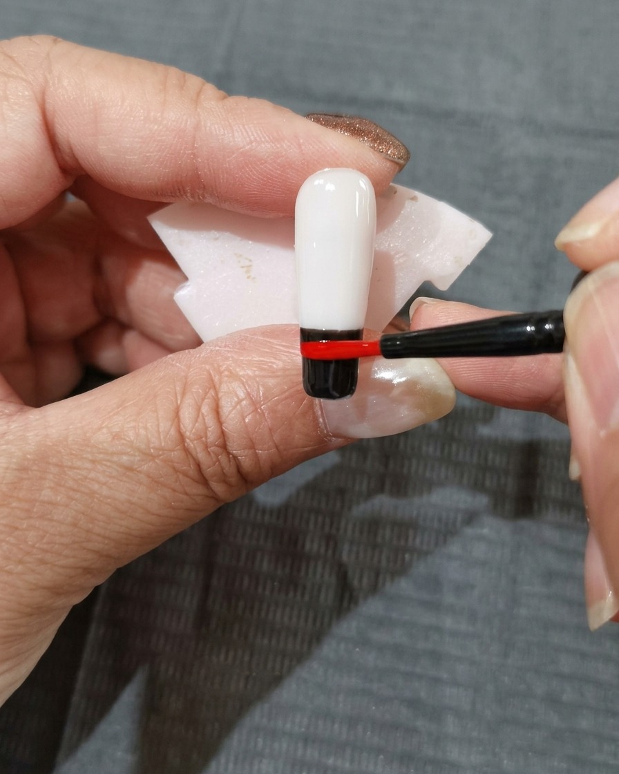 Una franja de esmalte de gel rojo anaranjado colocada justo encima de la banda roja en la uña.