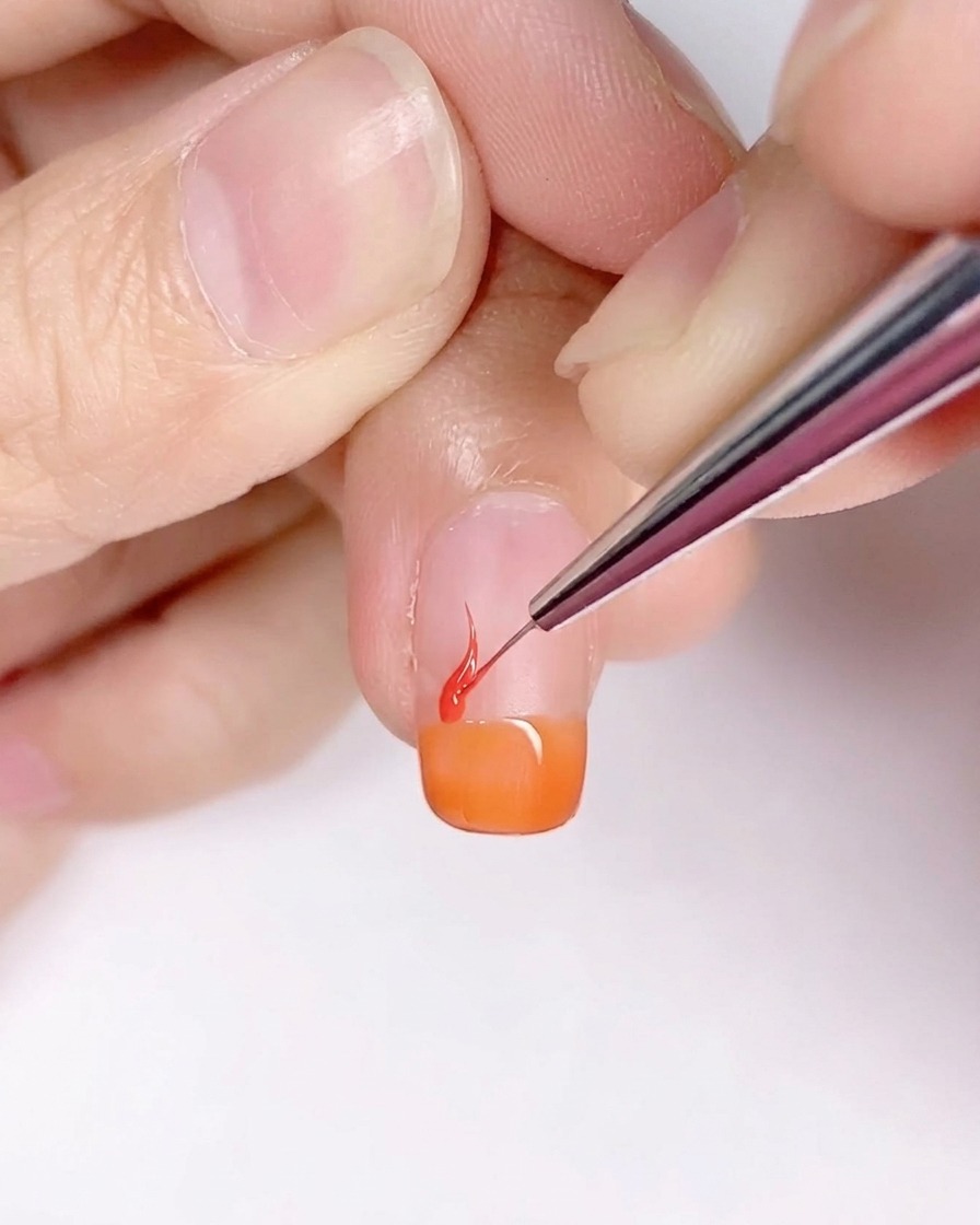 Pincel fino de detalle creando formas de flamas sobre la base naranja de la uña.