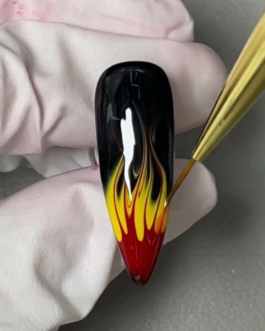 Un pincel aplicando una capa fina de blooming gel transparente sobre una base de uña negra brillante.