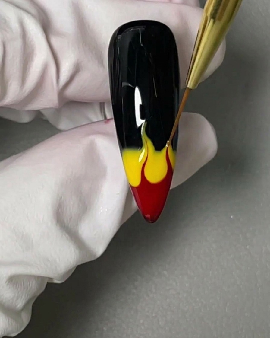Un pincel liner fino arrastrando los geles rojo y amarillo hacia arriba para formar siluetas de llamas.