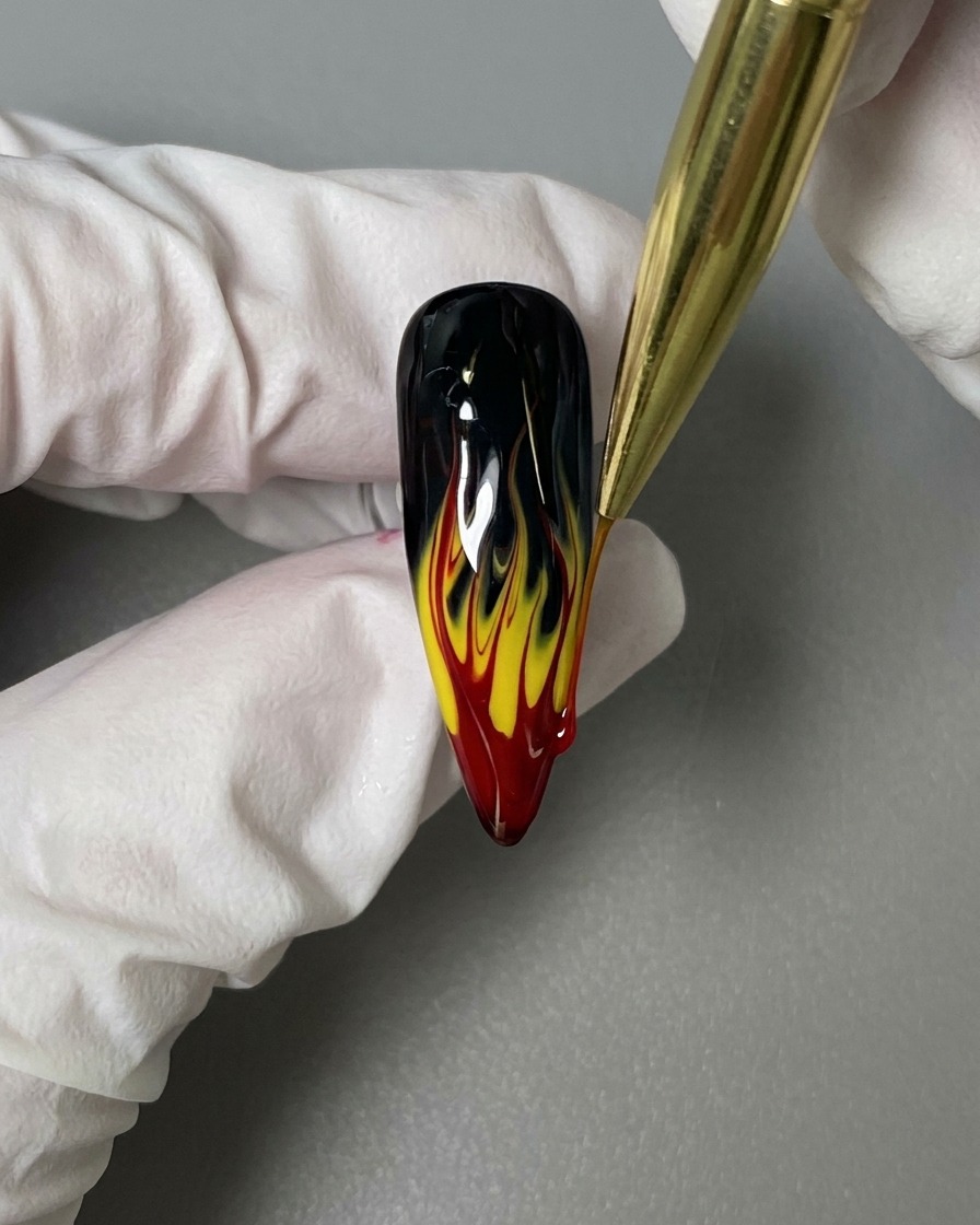 Un pincel liner aplicando una capa de brillo final sobre el diseño de uñas terminado.