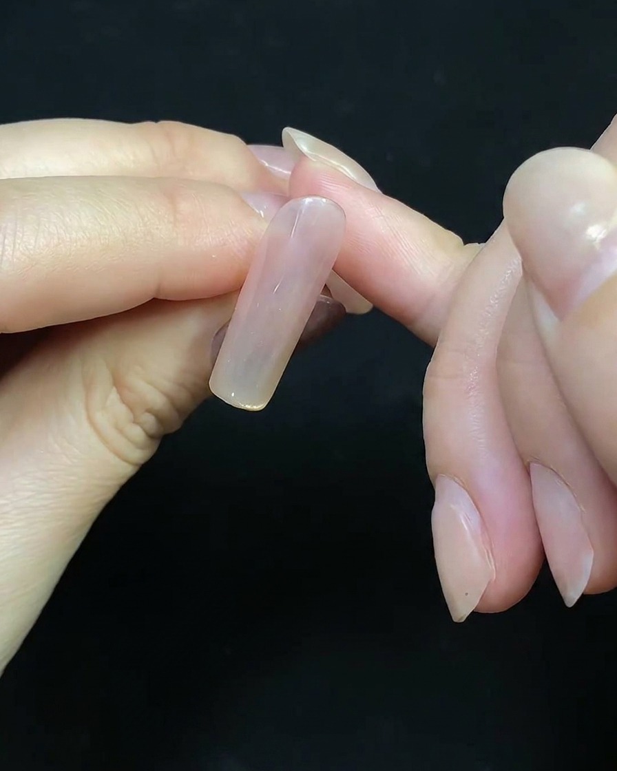 Un pincel fino de detalle dibujando líneas rojas delicadas sobre una uña para crear un diseño de fuego artificial.