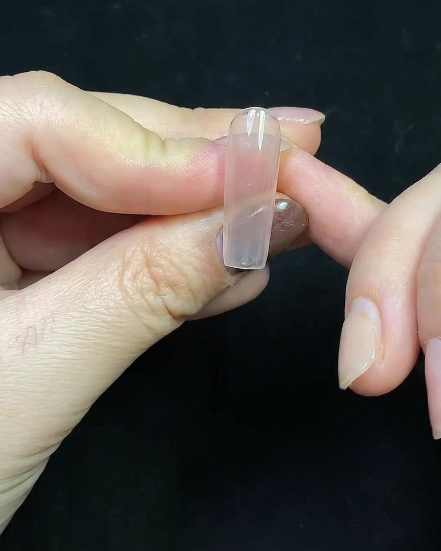 Primer plano de una punta francesa de gel rojo profundo siendo pintada sobre una extensión de uña transparente.