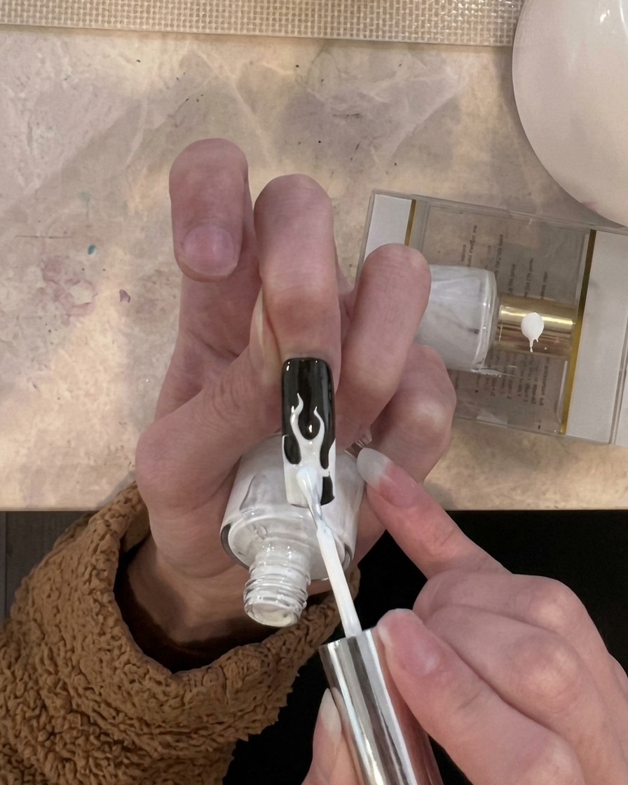 Un pincel aplicando una capa de esmalte en gel blanco específicamente en las áreas de las llamas en la punta de la uña.