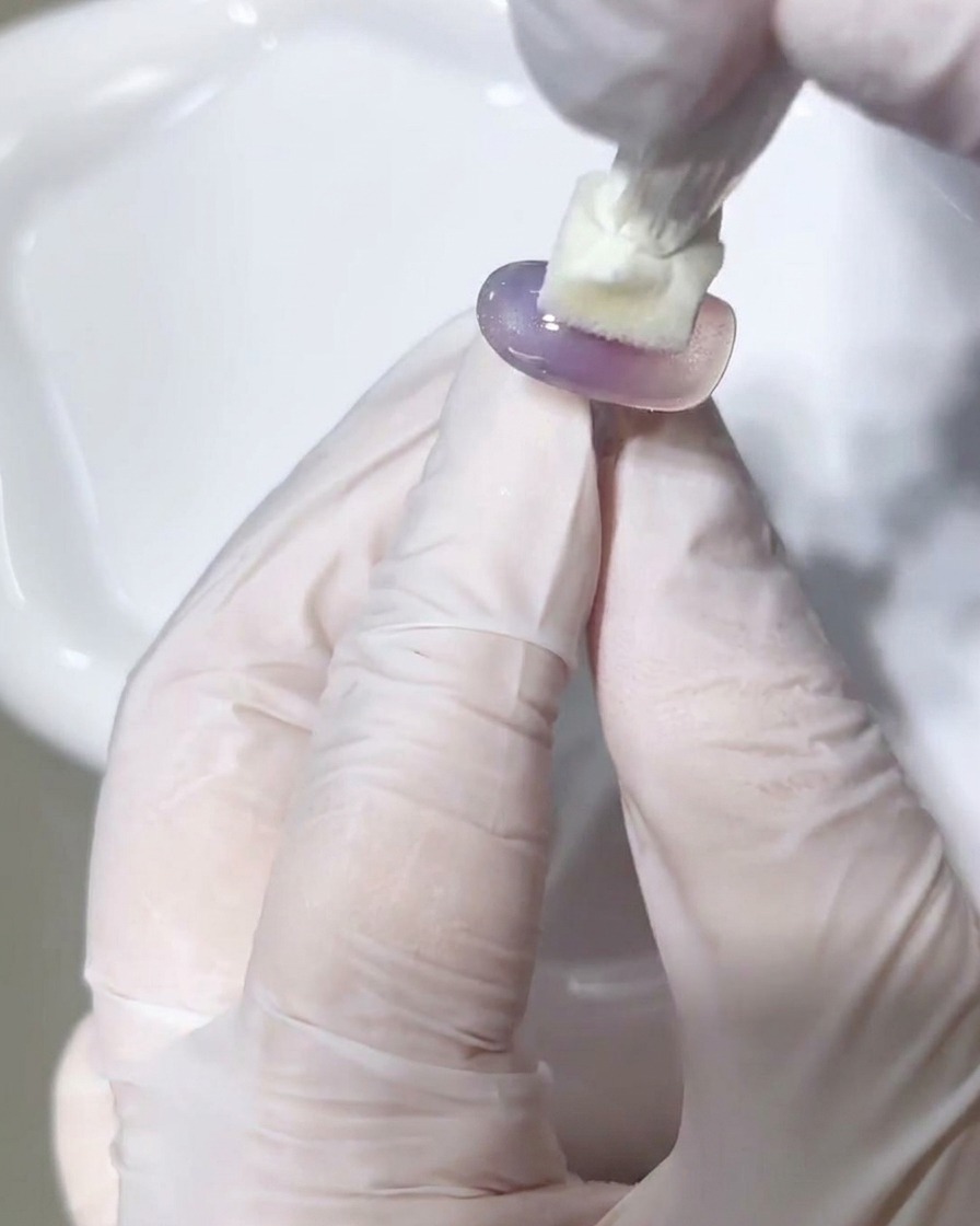 Una toallita sin pelusa limpiando la superficie de un tip de uña de gel curado.