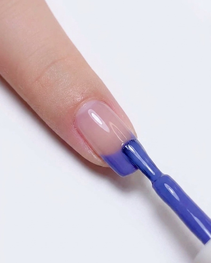 Volviendo a aplicar esmalte de gel azul y morado en la punta de la uña para intensificar la transición de color.