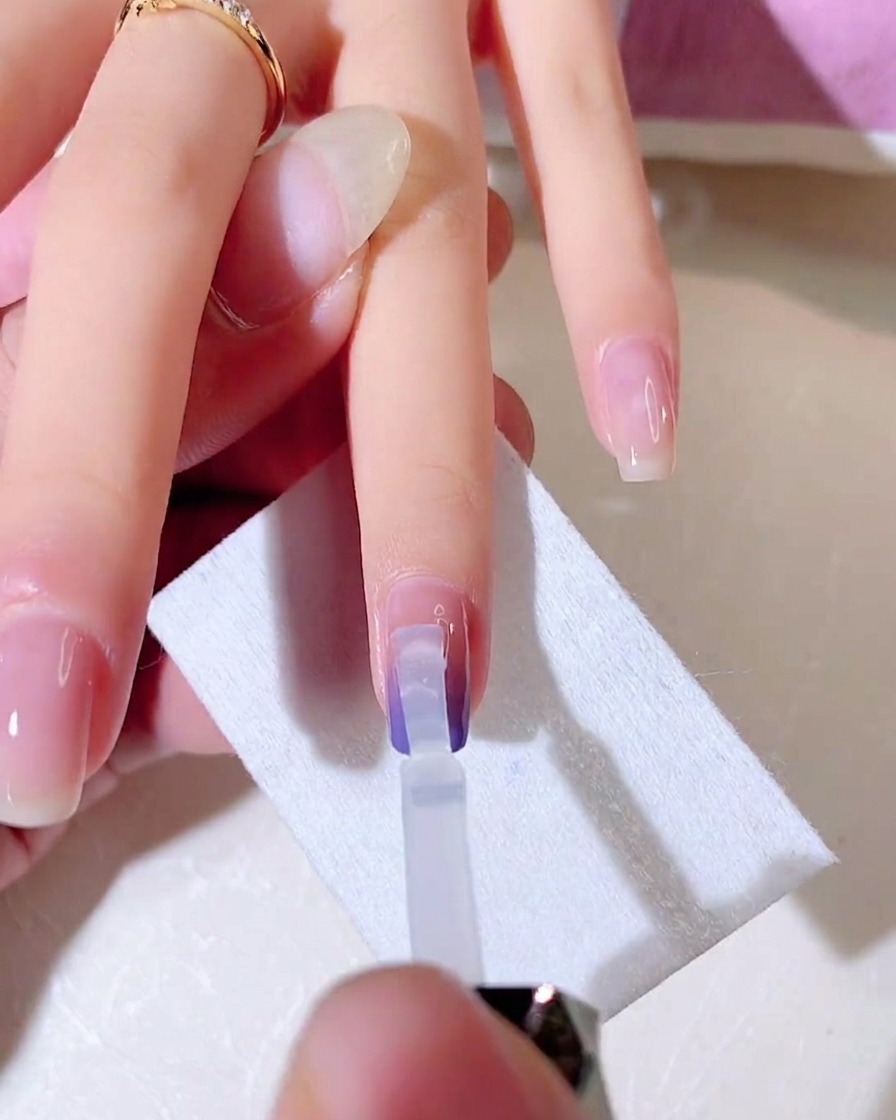 Un pincel de gel transparente difuminando la segunda capa de color degradado hacia abajo en la uña.