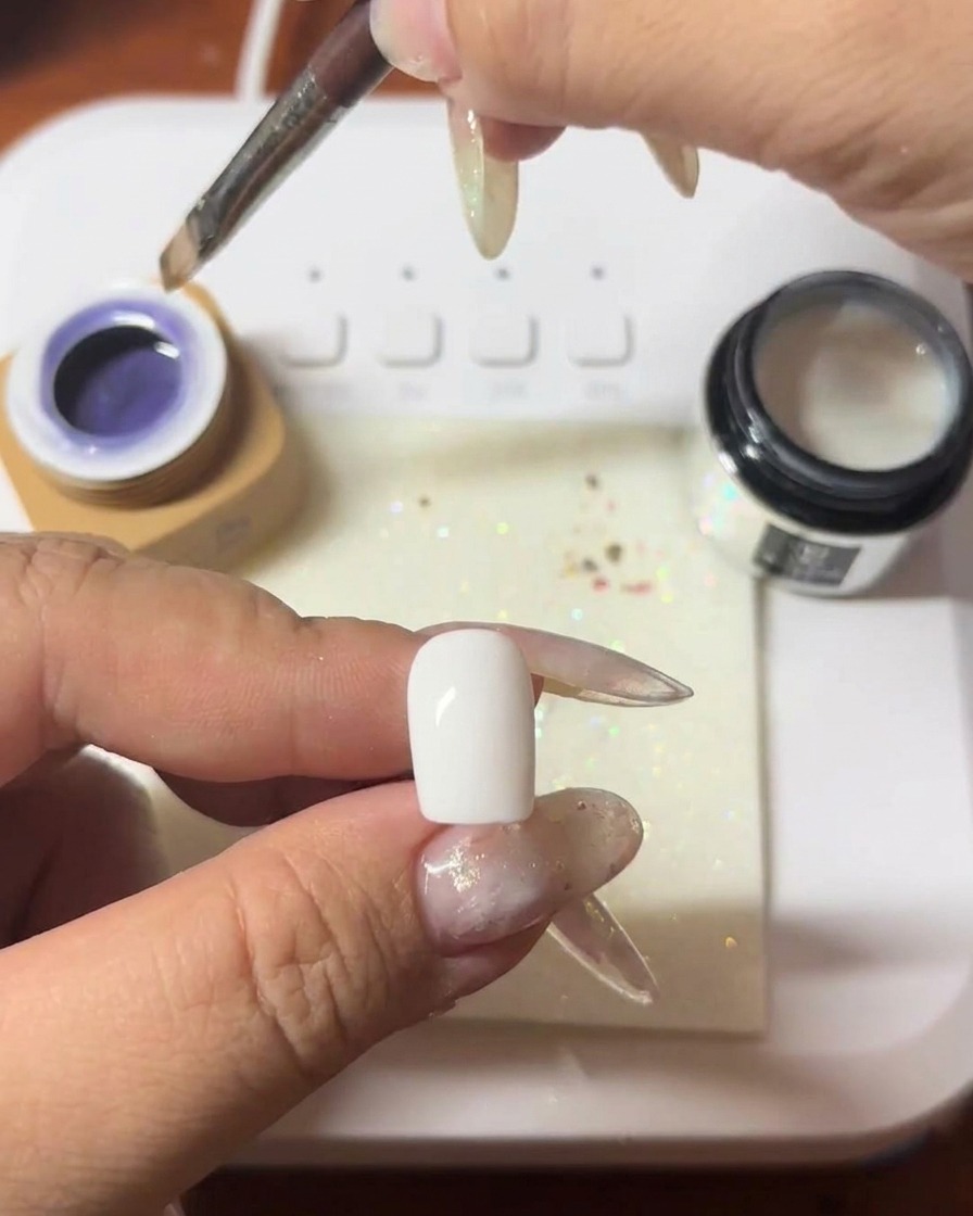 Un pincel aplicando una capa de gel cat-eye morado intenso sobre una uña.