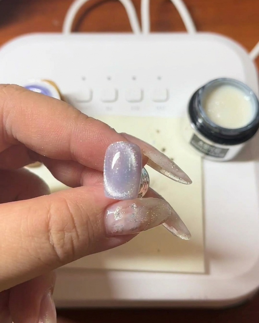Primer plano de un imán sobre una uña con gel morado formando una línea brillante.