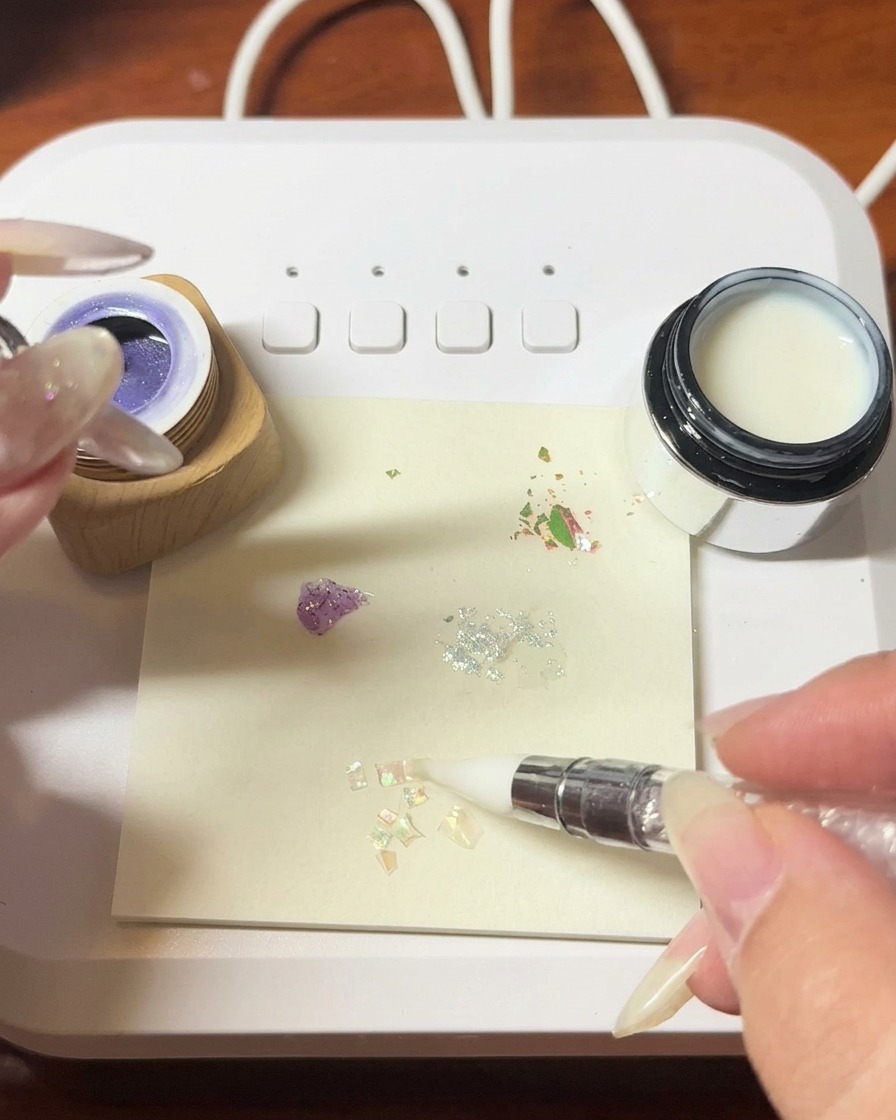 Pinzas colocando fragmentos de concha iridiscente sobre la superficie de gel húmedo.