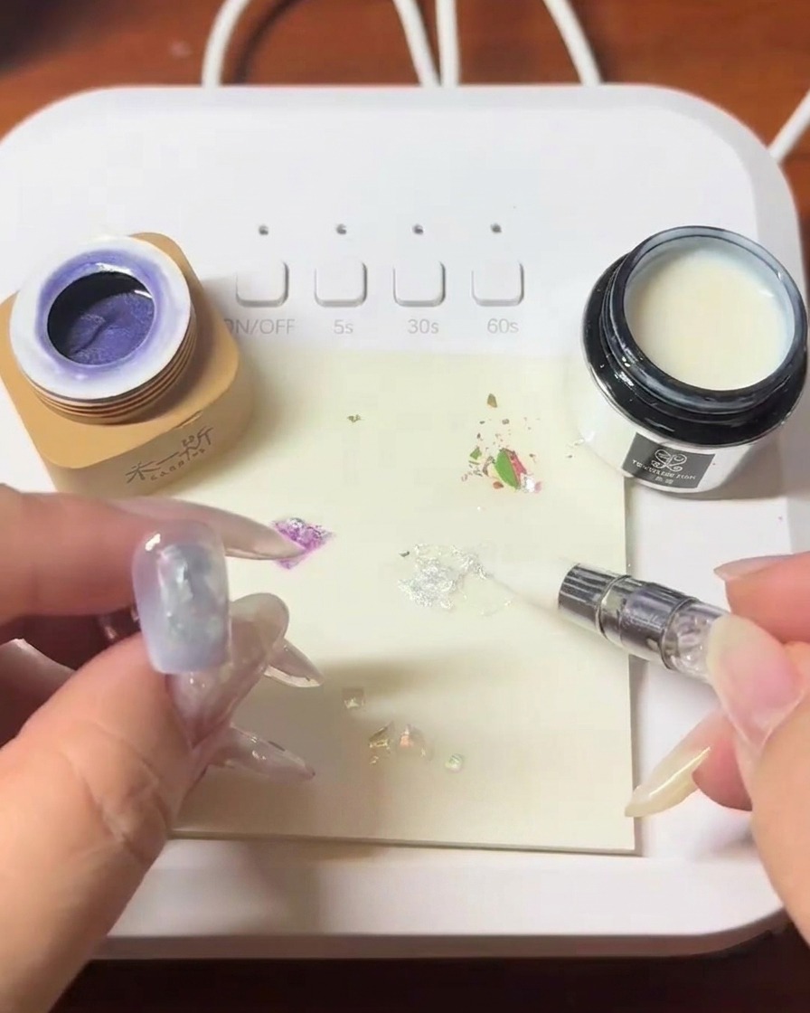 Un pincel aplicando una capa de blooming gel transparente sobre la uña decorada.
