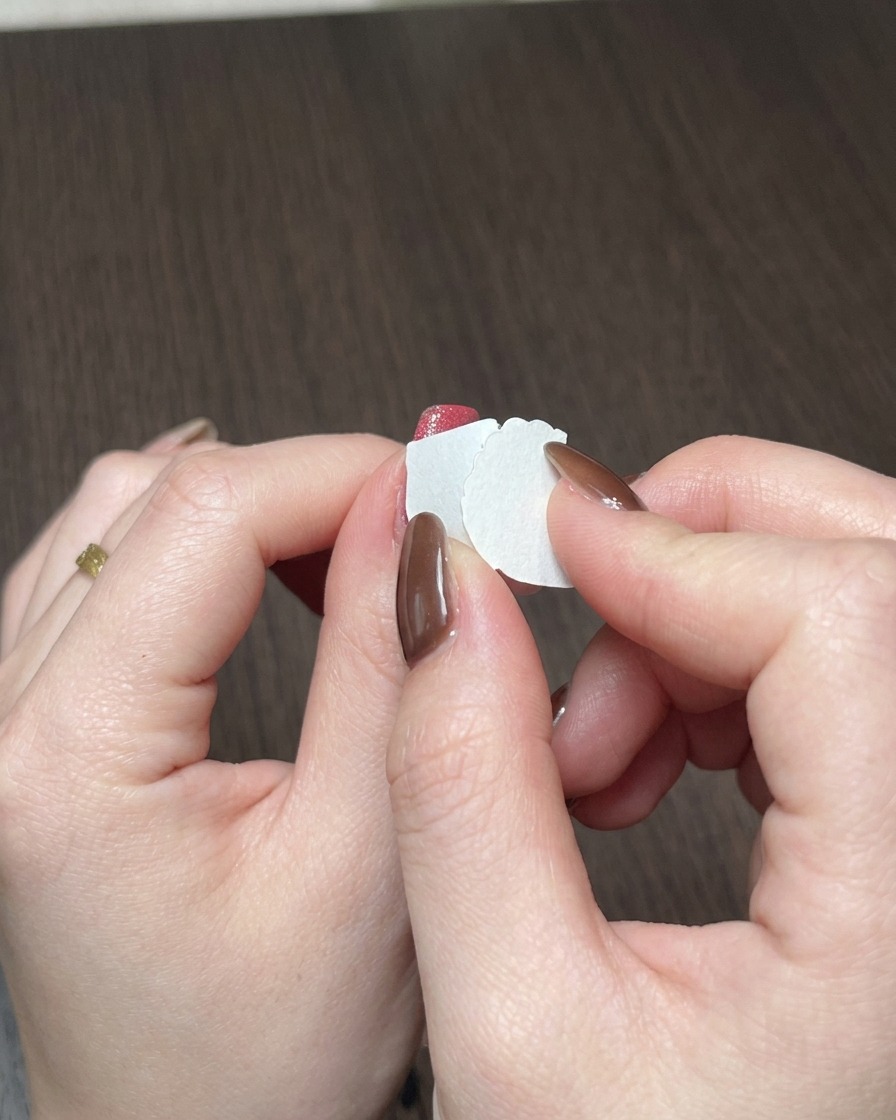 Primer plano de una esponja de maquillaje aplicando esmalte de gel rojo a toquecitos en el borde libre de una uña.