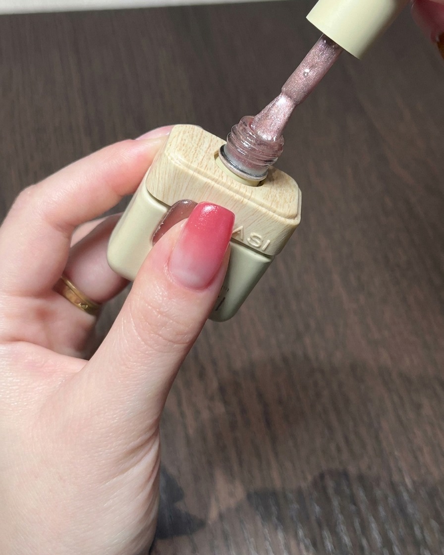 Un pincel aplicando un gel cat eye rosa nude brillante sobre la base degradada roja.