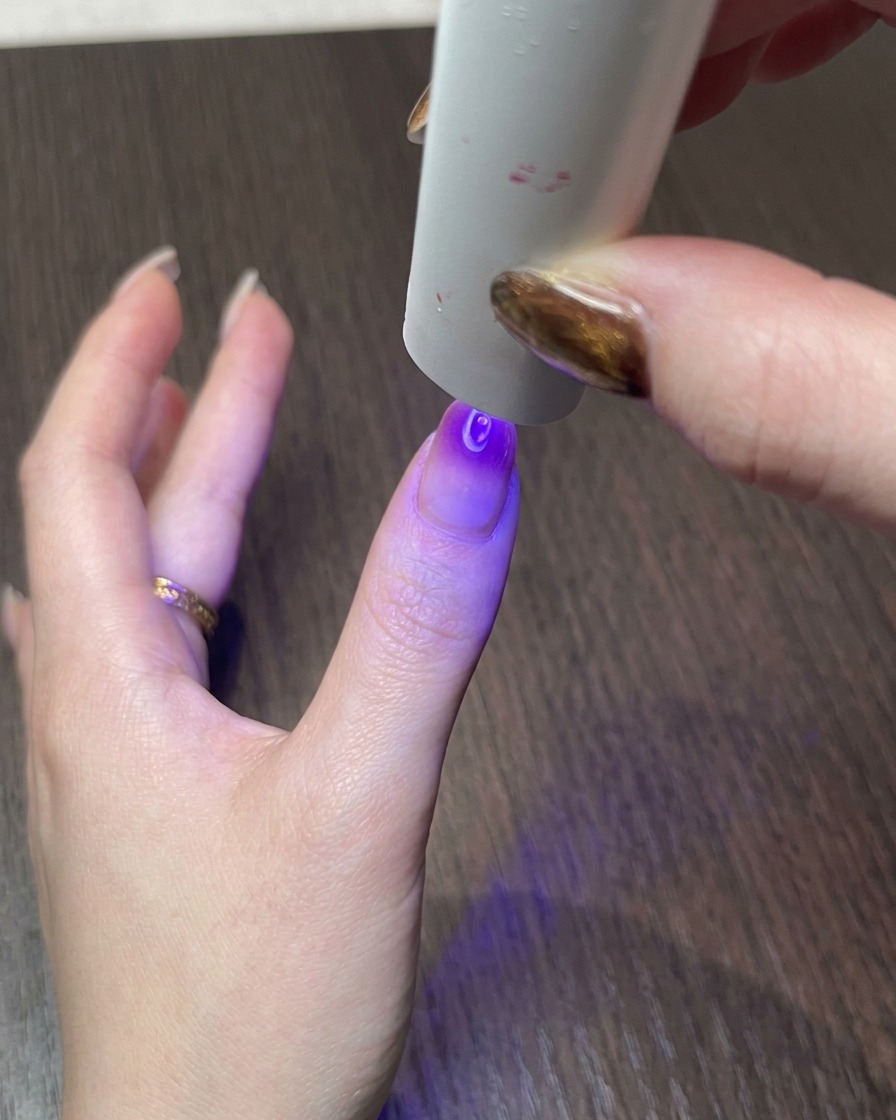 Una mano bajo una pequeña lámpara UV, curando el diseño magnético cat eye terminado.