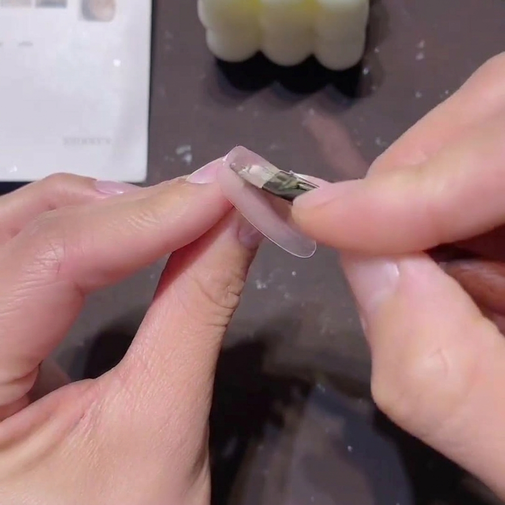 Un pincel aplicando una capa fina de esmalte en gel rosa nude translúcido sobre una uña preparada.