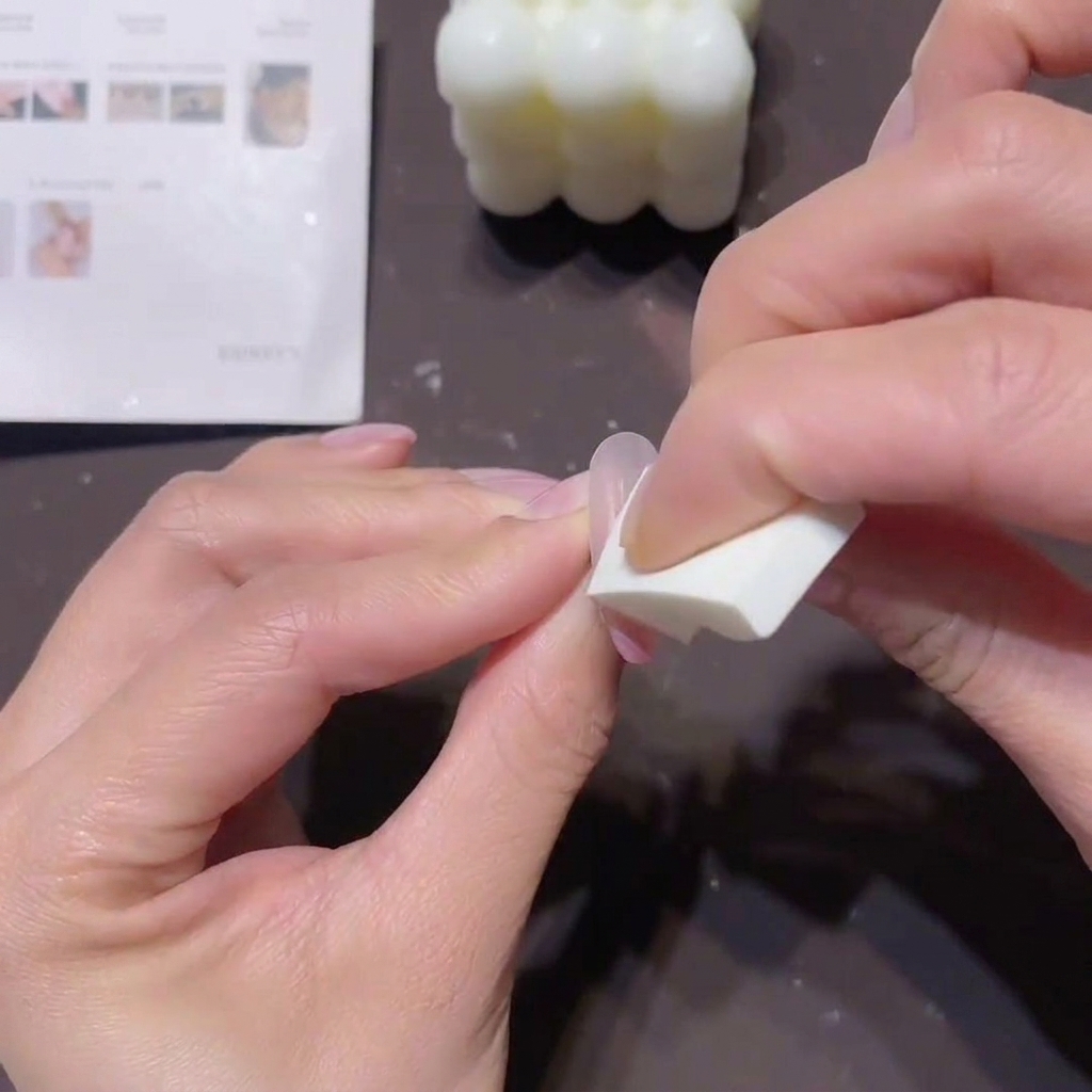 Primer plano de manos usando una pequeña esponja de cuña blanca para aplicar gel color melocotón-rosa en la punta de una uña para crear un efecto ombré.