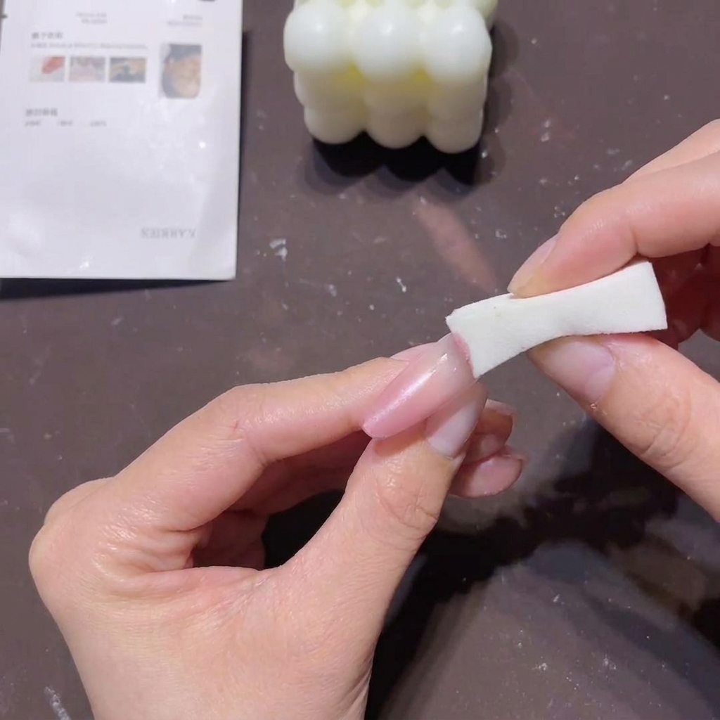 Primer plano de una mano usando un bloque de esponja blanca para aplicar gel melocotón-rosa en la punta de una uña larga para crear un efecto degradado.