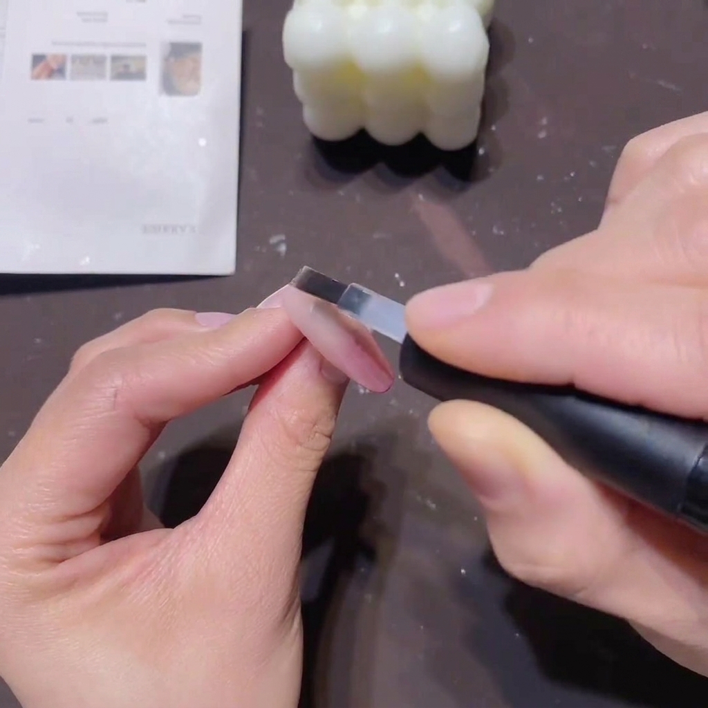 Un pincel plano aplicando una capa suave de base coat transparente sobre una uña con degradado rosa para sellar el color.