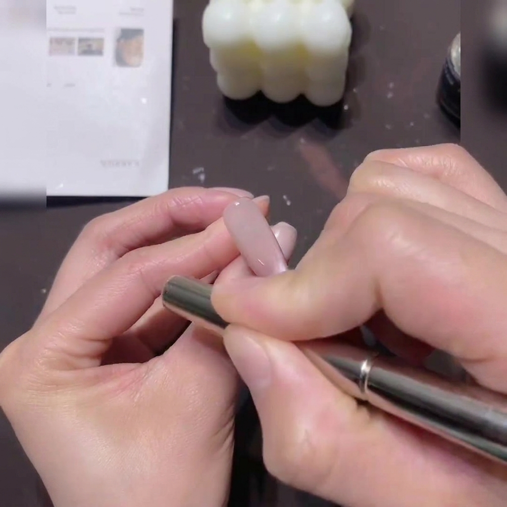 Una mano sosteniendo un imán cilíndrico, manteniéndolo en movimientos circulares alrededor del borde de una uña recubierta con gel Cat-Eye.