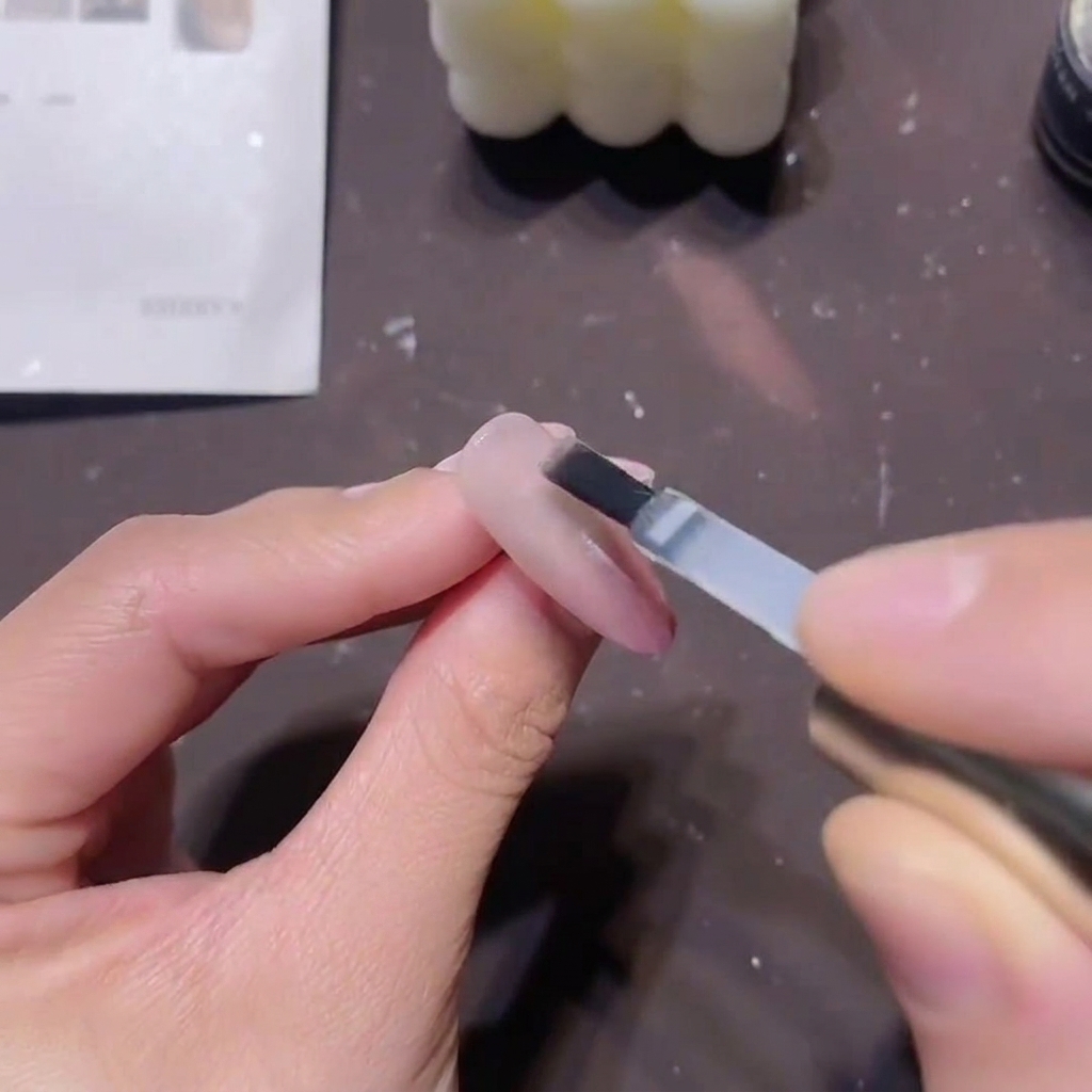 Un pincel de gel plano aplicando un builder top coat espeso y transparente sobre un diseño de uñas rosa magnético terminado.