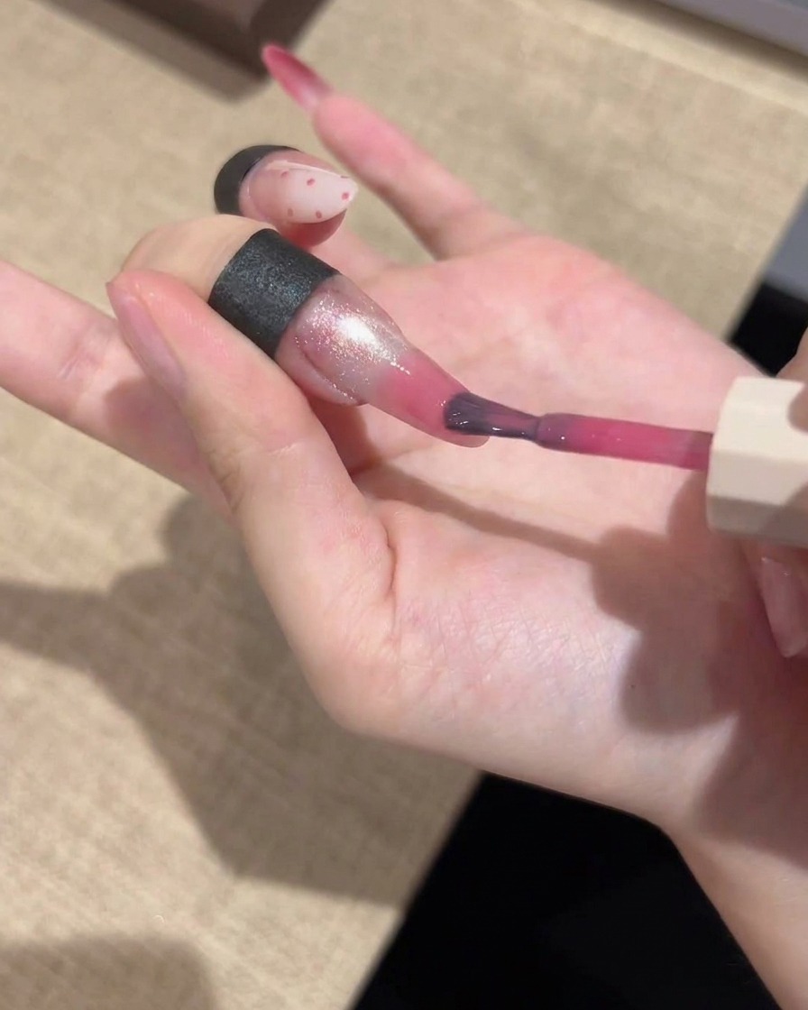Un pincel de detalle fino aplicando un color de gel rosa vibrante en las puntas de una uña manicurada, difuminándolo para un acabado degradado.